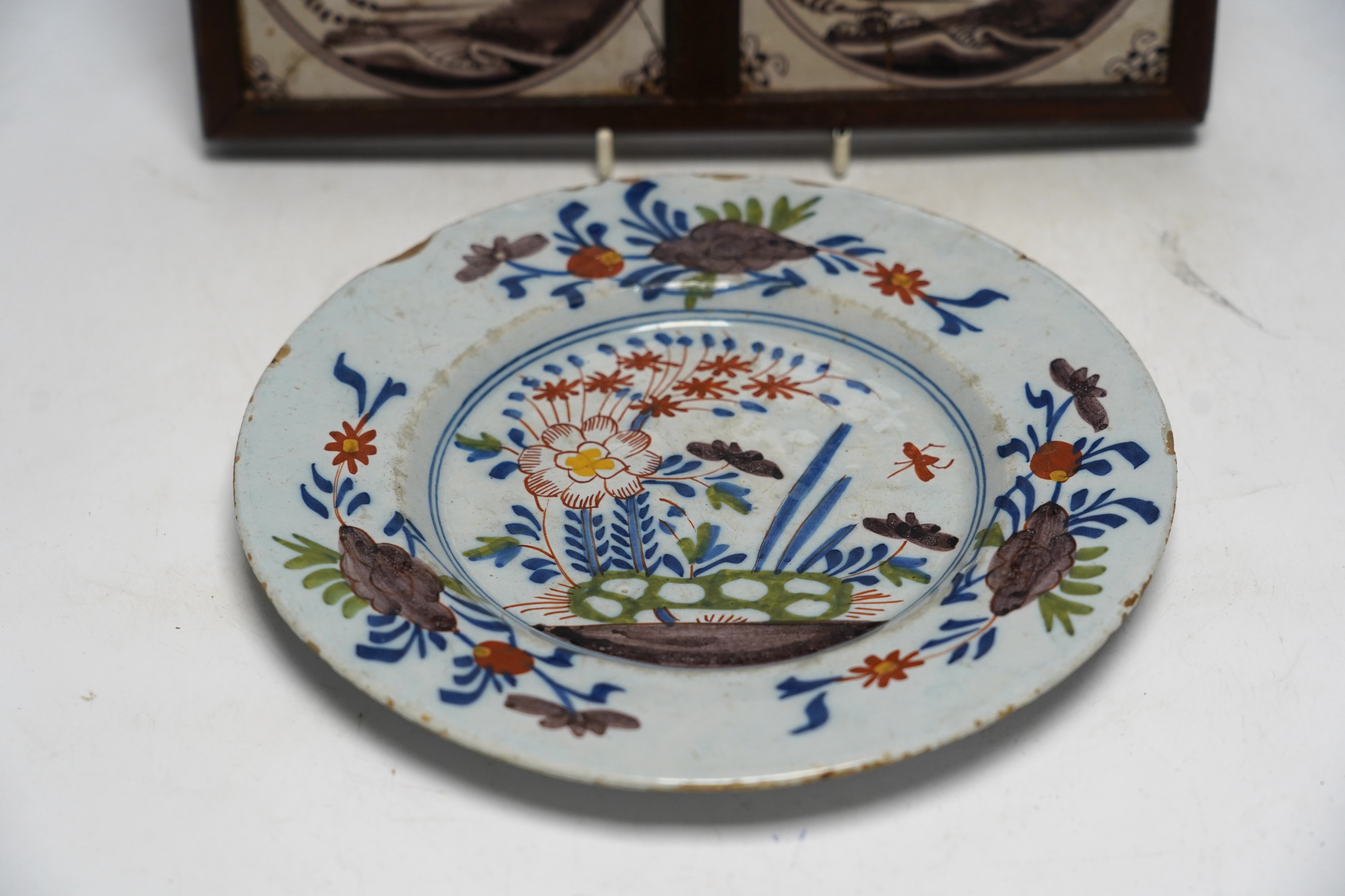 An 18th century Delft polychrome plate, 23cm diameter, and two framed tiles. Condition - tiles poor, plate with usual chipping to edges